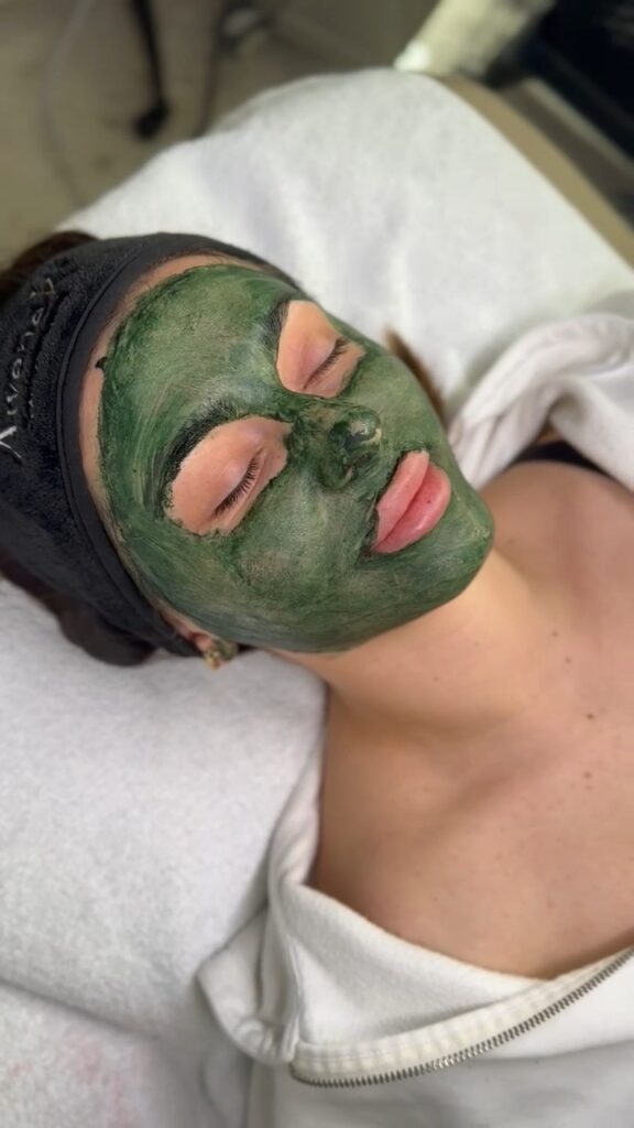 Eine Person mit geschlossener Augen trägt eine grüne Gesichtsmaske und ein Stirnband.