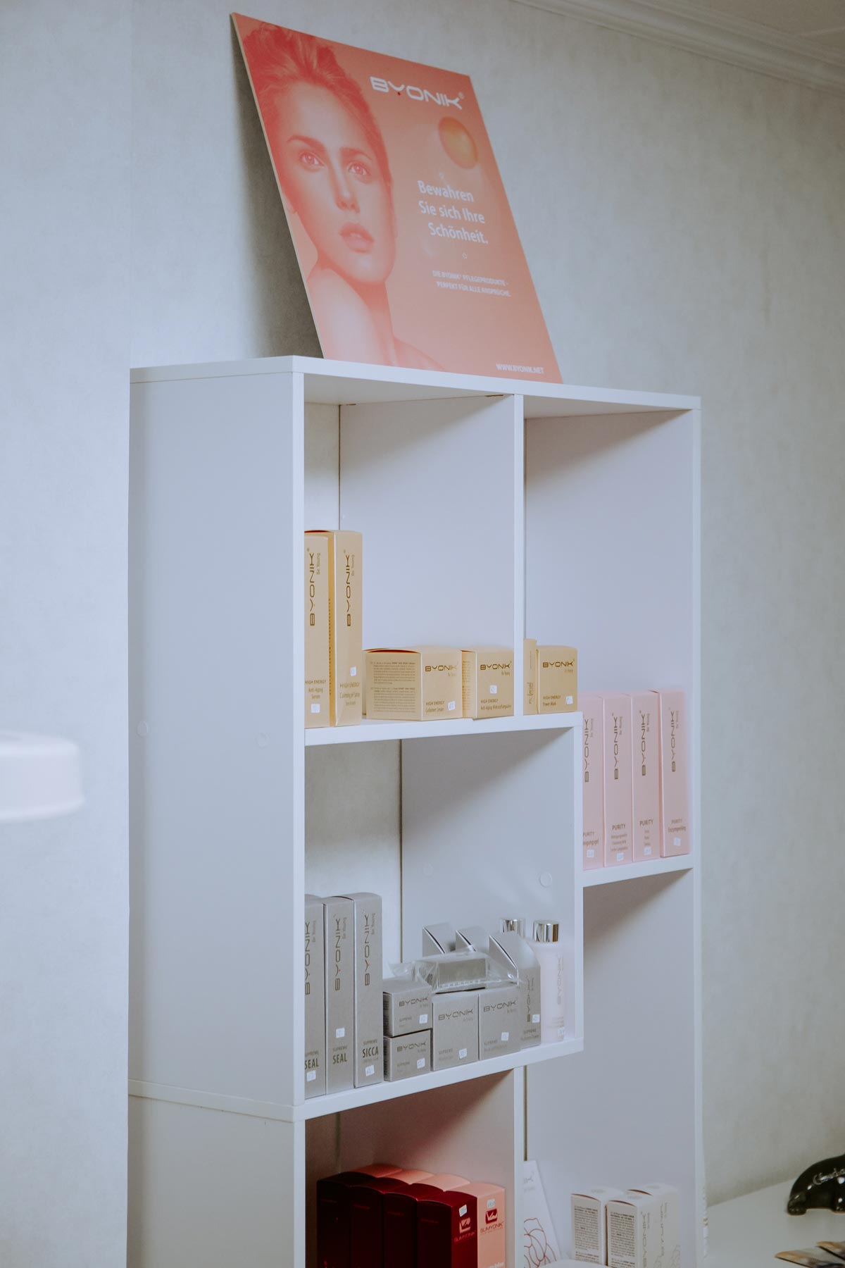 Ein weißes Regal mit kosmetischen Produkten und einem Werbeplakat oben.
